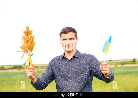 Recentrer le jeune homme portant le drapeau ukrainien et les épis de blé de blé attachés et le drapeau sur le fond de la nature du pré. Drapeau de l'Ukraine. Liberté. Les hommes ukrainiens Banque D'Images
