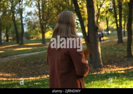 Recentrer le portrait d'une femme blonde de race blanche d'âge moyen dans le parc d'automne. Femme brillante et élégante en manteau orange et châle de cou marchant en octobre p Banque D'Images