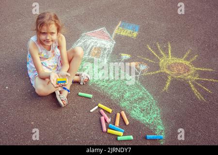 Une fille ukrainienne dessine les dessins des enfants avec de la craie sur le trottoir. Banque D'Images