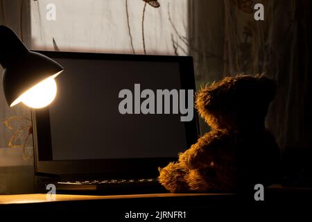 ours en peluche pour enfants assis portant un ordinateur portable sur la table, portant une lampe de table dans les chambres la nuit, portant des fenêtres, solitude, joie dans une la Banque D'Images