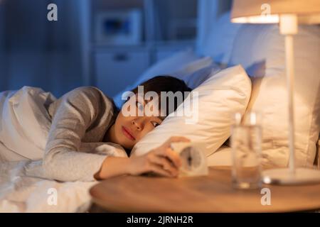 femme asiatique avec horloge couchée au lit la nuit Banque D'Images