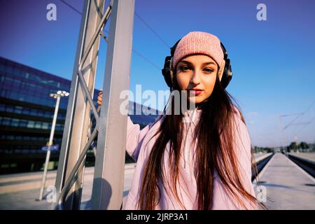 Une jeune fille avec un casque sur la construction métallique d'une gare est en train de regarder vers la caméra. Banque D'Images