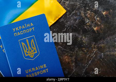 Passeport biométrique ukrainien et drapeau ukrainien sur fond sombre. Émigration, voyages, tourisme, vol de la guerre en Ukraine, identification. Le Banque D'Images