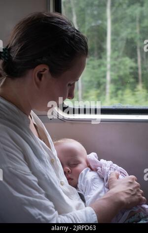 Bébé caucasien dormant en train sur les genoux de la mère Banque D'Images