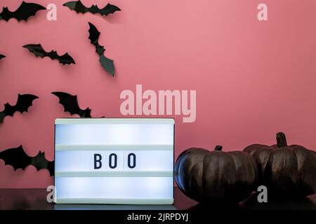Halloween Party Decor, Light Box avec texte Boo , citrouilles noires et silhouettes de chauve-souris sur le mur rose Banque D'Images