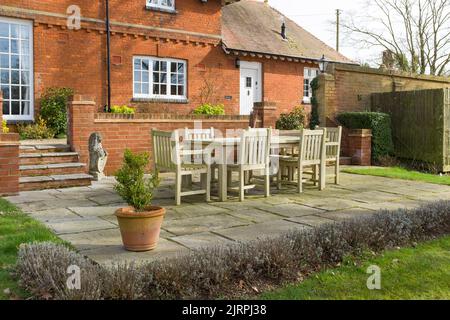 Jardin patio en hiver dans un jardin anglais. Terrasse pavée avec mobilier en teck à l'extérieur d'une ancienne maison de caractère, Royaume-Uni Banque D'Images