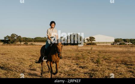 un jeune cavalier souriant part au coucher du soleil sur son cheval marron Banque D'Images