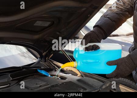 Gros plan de gants conducteur ou mécanicien versant du liquide antigel bleu pour le lavage de pare-brise de voiture d'hiver avec arrosoir bootle Banque D'Images