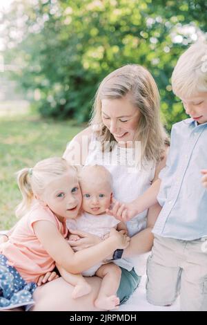 Blonde, la mère caucasienne est assise avec trois enfants dans le parc souriant. Banque D'Images