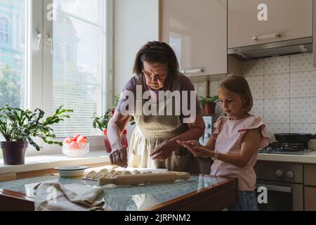 La grande-grand-mère et la petite-fille cuisinent des tartes dans la cuisine. Banque D'Images