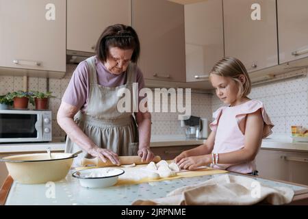 La petite-fille aide la grand-mère à faire des tartes dans la cuisine. Banque D'Images