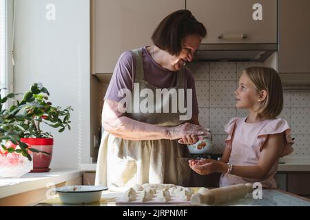 La grande-grand-mère et la petite-fille cuisinent des tartes dans la cuisine. Banque D'Images