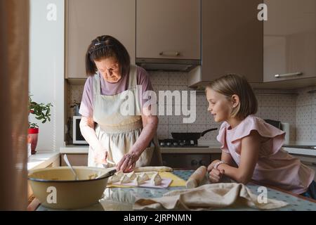 La grande-petite-fille regarde comme la grande-grand-mère cuisine des tartes. Banque D'Images