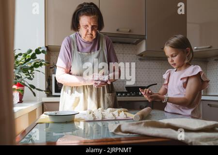 La petite-fille aide la grand-mère à cuisiner des tartes dans la cuisine. Banque D'Images