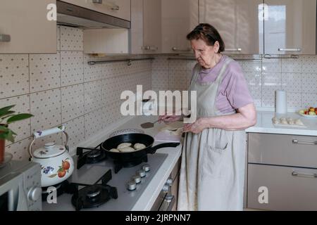 Une femme âgée friture des tartes dans sa cuisine. Banque D'Images