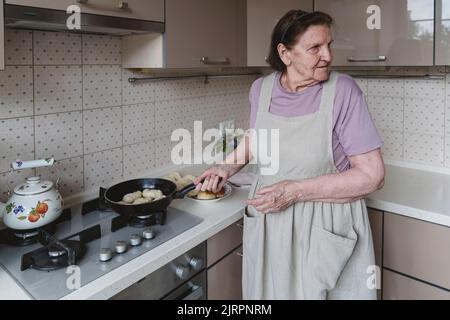 Une femme âgée dans la cuisine friture des tartes. Banque D'Images