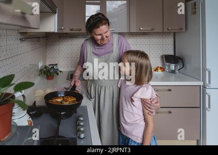 Une femme âgée avec sa petite-fille friture des tartes dans la cuisine. Banque D'Images