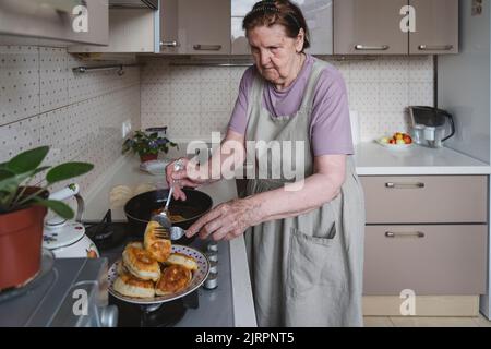 Une femme âgée friture des tartes dans la cuisine. Banque D'Images