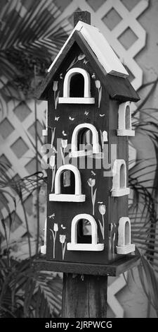 Un cliché vertical en niveaux de gris d'une maison d'oiseaux en bois avec un mur décoré de motifs Banque D'Images