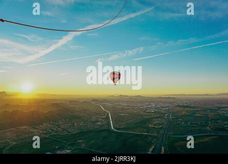 Un ballon d'air chaud flotte sur un paysage désertique calme mais magnifique, à motifs de routes et de maisons, tandis que le soleil se lève sur les montagnes Banque D'Images