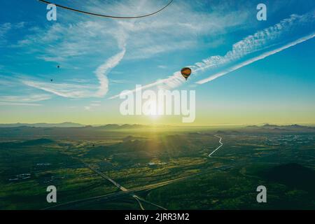 Un ballon d'air chaud flotte sur un paysage désertique calme mais magnifique, à motifs de routes et de maisons, tandis que le soleil se lève sur les montagnes Banque D'Images