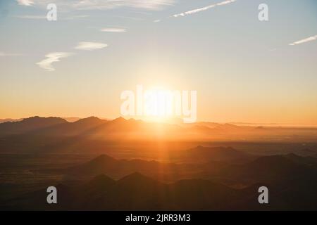 Le soleil orange flamboyant s'élève sur une gamme de montagnes tôt le matin, ce qui les fait ressembler à des ombres Banque D'Images