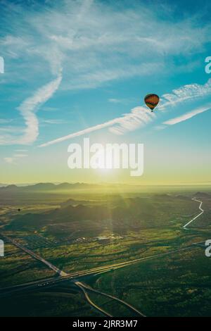 Un ballon d'air chaud flotte sur un paysage désertique calme mais magnifique, à motifs de routes et de maisons, tandis que le soleil se lève sur les montagnes Banque D'Images