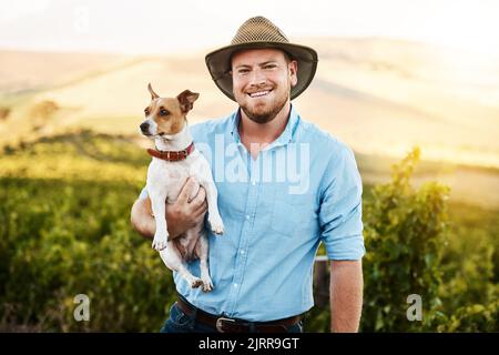 Nous avons tous les deux plaisir à travailler ensemble autour de la ferme. Portrait d'un agriculteur tenant son chien dans un vignoble. Banque D'Images