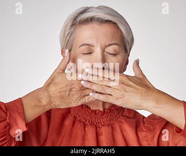 Senior, mains et bouche d'une femme âgée couvrant ses dents ou ses lèvres avec la main contre un fond gris de studio. Femme mature et vieillissante Banque D'Images