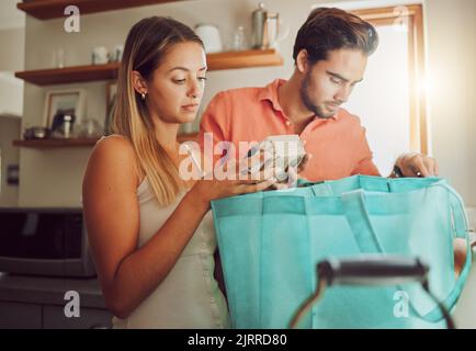 Articles d'épicerie, sans plastique et un couple sain se déballer après avoir retourné à la maison après un voyage de shopping. Homme et femme sérieux avec sac réutilisable avec nourriture et Banque D'Images