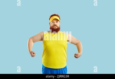 Drôle sérieux gros homme montrant des muscles après l'entraînement sportif sur fond bleu clair. Banque D'Images