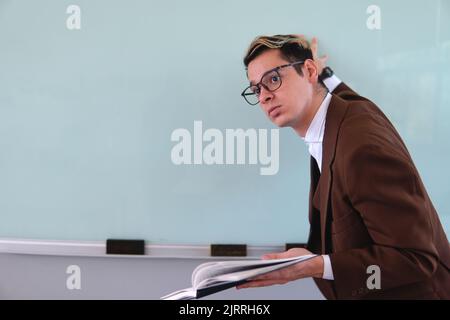 Professeur élégant. Homme blanc blond habillé avec élégance dans une veste, une chemise et des verres bruns. Homme vêtu d'un sac devant un groupe scolaire. Photo de haute qualité Banque D'Images