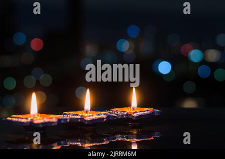 Mise au point sélective sur la flamme des premières lampes diya d'argile éclairées sur fond sombre avec des lumières bokeh colorées. Concept du festival Diwali. Banque D'Images