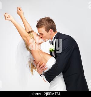 L'amour, le mariage et le couple heureux baiser à leur réception de mariage sur un fond blanc de studio. Homme, femme ou mariée et marié en célébration de leur Banque D'Images