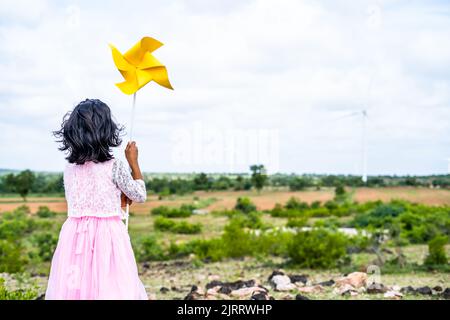 Vue arrière prise de vue de fille enfant jouant le carton ventilateur de papier à l'éolienne - concept de la liberté, le style de vie d'enfance et le développement. Banque D'Images