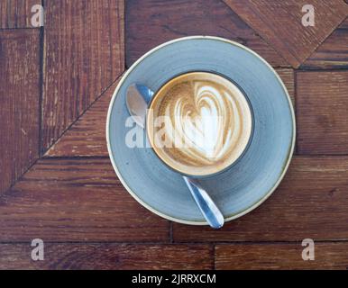 Une tasse de café blanc plat avec soucoupe et cuillère sur fond de bois sombre Banque D'Images