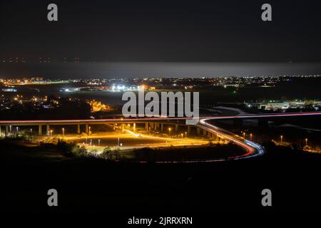 Light Trails avec des voitures, Shoreham aéroport et la côte dans le milieu du sol et la mer au clair de lune en arrière-plan. Banque D'Images