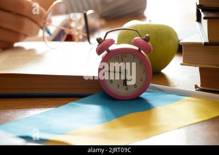 Un réveil se tient sur une table près des livres et une pomme sur les drapeaux de l'Ukraine, l'éducation scolaire en Ukraine, le temps d'étudier, l'éducation en Ukraine Banque D'Images