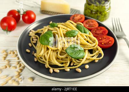 Pesto de pâtes avec fourchette sur fond de bois blanc. Spaghetti italiens traditionnels avec ingrédients alimentaires sauce pesto, tomate, parmesan, pignons de pin, Banque D'Images