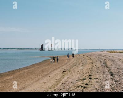 Promenade sur la plage à Bradwell Waterside et deux barges de voile rouges historiques sur la Tamise sur l'estuaire de Blackwater, Bradwell on Sea, Essex, Angleterre Banque D'Images