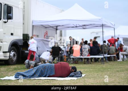 Ter Apel, pays-Bas. 26th août 2022. Un homme se trouve devant un centre d'asile, à l'arrière-plan une station de traitement de l'organisation "Doctors without Borders" a été construite. Médecins sans frontières pour la première fois traitent également les gens aux pays-Bas - au centre national d'asile Ter Apel, où depuis des semaines des centaines de demandeurs d'asile dorment en plein air dans les environs de l'installation après la frontière avec la Basse-Saxe, pour le manque de places de couchage dans l'installation. Crédit : Lars Klemmer/dpa/Alay Live News Banque D'Images