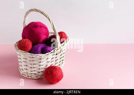 Boules de fil roses et rouges dans un panier sur fond rose, Hobby Banque D'Images