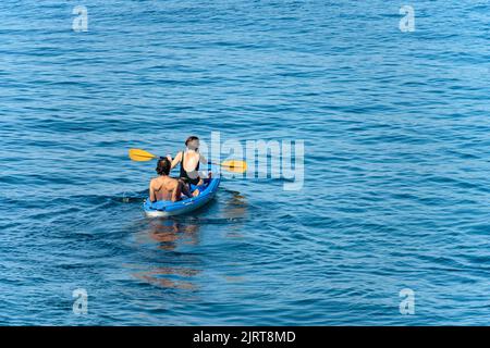 Un couple d'âge mûr à bord d'un kayak bleu, pagayant dans la mer Méditerranée bleue, par une journée d'été ensoleillée. Golfe de la Spezia, Ligurie, Italie, Europe du Sud Banque D'Images