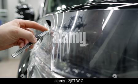 Le maître coupe le film de protection sur la voiture avec un couteau. Détails de voiture. Homme spécialiste appliquant le film de coloration de fenêtre sur la voiture et coupe les exces Banque D'Images