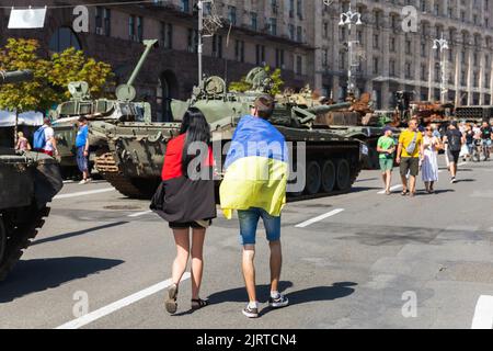 KIEV, UKRAINE - 24 août 2022: Un jeune couple couvert de drapeau de l'Ukraine et de drapeau des nationalistes ukrainiens, marche le long de Khreshchatyk parmi l'équipement militaire russe brûlé Banque D'Images