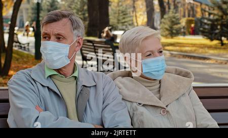 Couple de famille âgé dans des masques médicaux s'assoir à l'automne parc homme mature se détourne ressentiment croisant les bras conversation désagréable à l'extérieur Banque D'Images