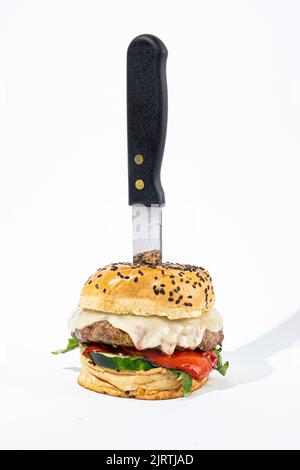 Un cliché vertical d'un cheeseburger avec un couteau sur fond blanc Banque D'Images
