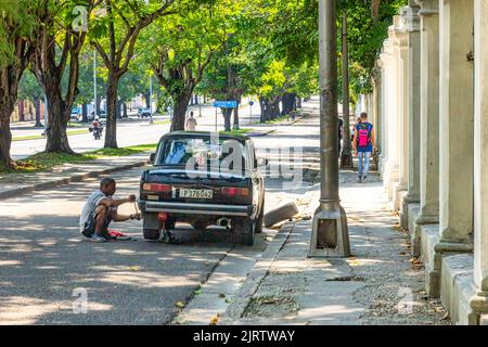 Un cubain change le pneu d'un véhicule russe dans une rue de la ville. Le trottoir à droite est endommagé ou manque d'entretien. Banque D'Images