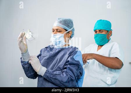 Infirmière aidant la femme chirurgien à porter une blouse d'opération pour la chirurgie - concept de profession professionnelle, carrière et personnel de soutien. Banque D'Images