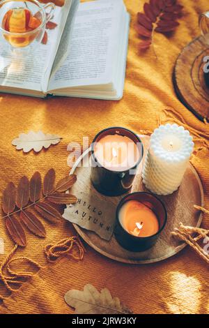 Bougies allumées avec carte hello automne, tisane dans verre tasse et livre ouvert sur le écossais jaune. Lecture, détente, loisirs à la maison. Ambiance d'automne. T Banque D'Images